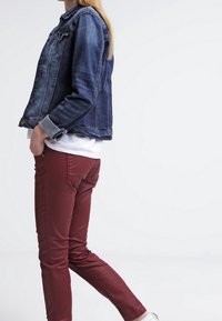 Jeansjacka i mörkblått, med knappstängningar och bröstfickor. Sammanvänt med åtsittande vinröda byxor och vit skjorta, visad från sidan.