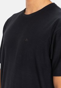 T-shirt in cotone nero con colletto a girocollo, maniche corte e finitura testurizzata sottile. Presenta un piccolo logo scuro nell'area sinistra del petto.