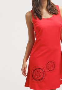 Rotes ärmelloses Kleid aus glattem Stoff, mit lasergefertigten kreisförmigen Mustern am Saum und einem runden Ausschnitt.