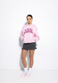 Pink hoodie with "LOCAL HEROES" text, paired with a black pleated mini skirt. Accessories include white socks and pink pointed-toe flats.