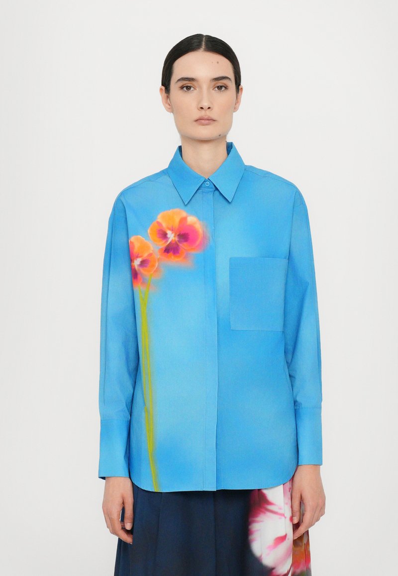 Light blue long-sleeve shirt with a collar, featuring a vibrant floral print in orange and pink on the front, and a breast pocket.