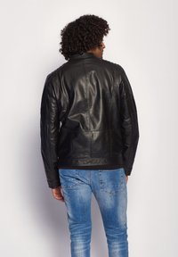 Sort læderjakke med teksturerede skuldre, tætsiddende design og en subtil glans. Kombineret med blå denim jeans, set bagfra.