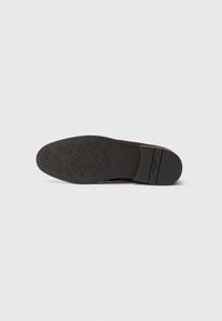 Suola di una scarpa elegante marrone con battistrada in gomma nera caratterizzato da motivi geometrici e con il nome del marchio "Heschung" sul tallone e al centro della suola.