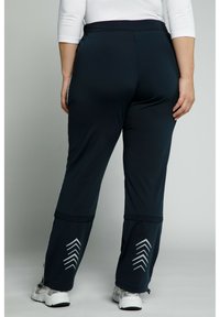 Námořnické sportovní kalhoty s hladkým povrchem, mají úzký pas, boční pruhy a reflexní vzory ve tvaru šípu blízko kotníků.