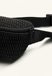 Rucsac negru de tip fanny, cu un model texturat împletit, închidere cu fermoar și curea ajustabilă. Material moale cu un finisaj mat.