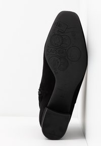 Semelle de chaussure formelle noire montrant un motif embossé avec des pièces, texte "KAISER" et talon texturé pour l'adhérence, sur fond blanc.