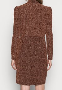 Robe à manches longues avec une taille cintrée, en tissu texturé marron avec un motif de petits points noirs. Longueur mi-cuisse.