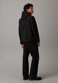 Giacca nera impermeabile con cappuccio, orlo elastico e texture liscia, abbinata a jeans neri a gamba dritta e stivali chunky.