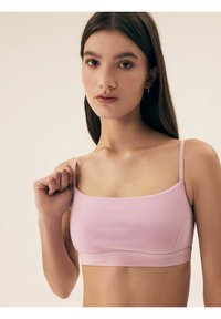 Jasnoróżowy biustonosz braletka z cienkimi ramiączkami, wykonany z gładkiego, elastycznego materiału i o kwadratowym dekolcie. Posiada detal szwu oraz dopasowany krój.