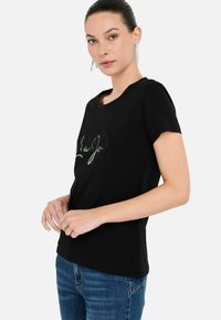 Zwarte t-shirt met korte mouwen, voorzien van een ronde halslijn en een glanzend, script-achtig logo op de voorkant. Gemaakt van zacht, glad materiaal.