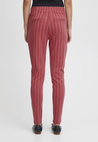 Pantaloni rossi con strisce verticali bianche, dotati di una vita elastica, due tasche posteriori e un design slim fit. Il tessuto appare liscio.