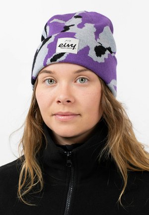 Paarse en grijze gebreide beanie met een zichtbaar merkembleem, gedragen boven een zwart fleece jack met ritssluiting. Zacht en gestructureerd materiaal.