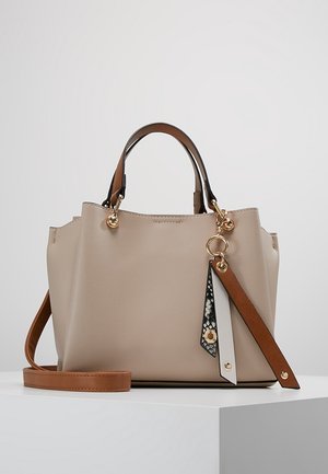 Beige leren handtas met bruine handvatten, afneembare schouderriem en decoratieve sleutelhanger van zwart, wit en bruin leer.