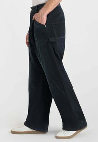 Zwarte denim wijde broek met een knoopsluiting, zijzakken en een gestructureerde afwerking, gecombineerd met witte sneakers met een beige zool.