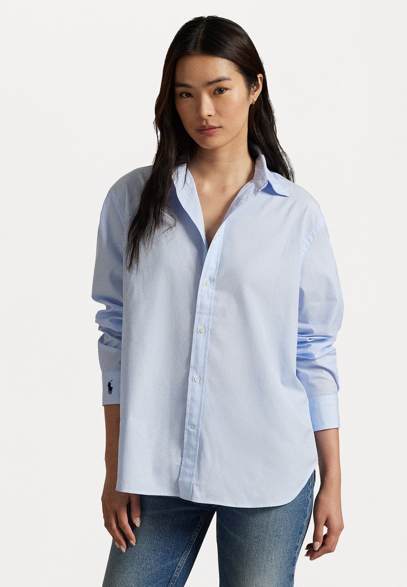 Chemise boutonnée bleu clair en coton avec un col classique, des manches longues et un petit logo brodé sur le poignet. Coupe décontractée.