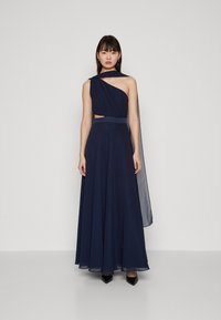 Robe navy avec une épaule asymétrique, tissu fluide, détail découpé à la taille et une longue cape translucide.