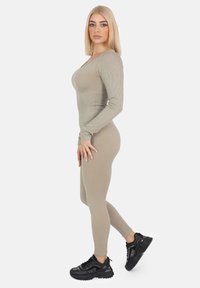 Khaki ribgebreide jumpsuit met lange mouwen, een ronde hals, een getailleerd silhouet, gecombineerd met zwarte chunky sneakers voor contrast.