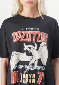 Black t-shirt featuring a vintage Led Zeppelin concert graphic. Design includes a white angel figure, bold text, and colorful accents.