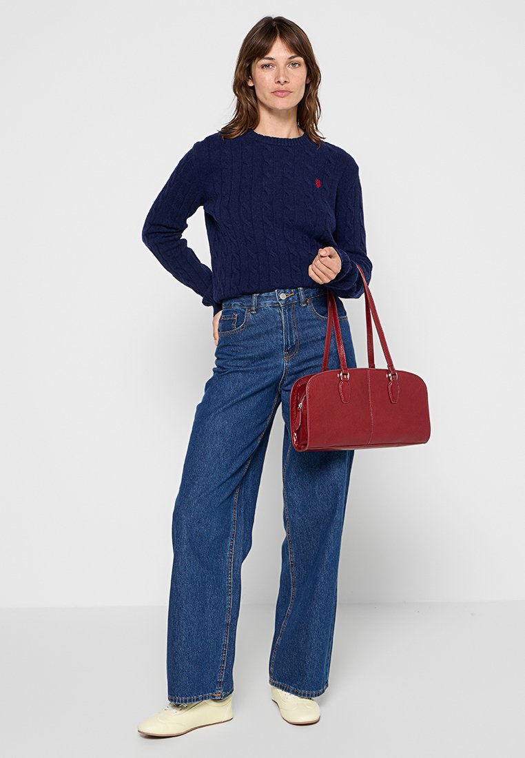 Marineblauer Karomuster-Pullover, hochtaillierte blaue Jeans, cremige Sneaker und eine rote Lederhandtasche mit zwei Griffen. Einfaches und funktionales Design.