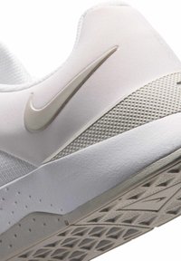 Λευκή φτέρνα αθλητικού παπουτσιού Nike με μπεζ λογότυπο Swoosh, υφασμένη ενδιάμεση σόλα και ανάγλυφη εξωτερική σόλα από ελαστικό, ορατή από πλάγια γωνία.
