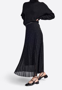 Jupe plissée noire avec des paillettes argentées, assortie à un pull noir et des chaussures à talons bas en cuir verni, avec des brides autour de la cheville.