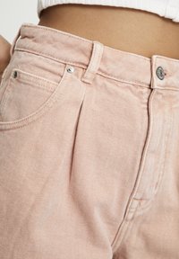 Pantalones de pana rosa claro con acanalado vertical, que cuentan con una cintura alta, un botón plateado y bolsillos laterales, mostrados desde la cintura hacia abajo.