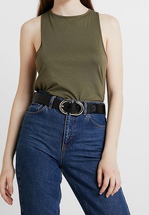 Oliivinvihreä hihaton toppi yhdistettynä korkeavyötäröisiin sinisiin farkkuihin ja mustaan keinonahkavyöhön, jossa on pyöreä hopeanvärinen solki.