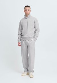 Lys grå hettejakke med glidelås, ribbestrikkede mansjetter og midje, kombinert med matchende joggebukser. Behagelig stoff, avslappet passform og elastisk midje.
