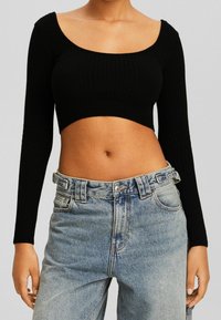 Svart ribbad croppad topp med vid rundad halsringning och långa ärmar, i kombination med ljusblå highwaisted jeans i denim.