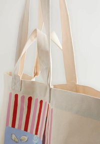 Plátená taška s dlhými popruhmi, ktorá má maľovaný dizajn farebných vertikálnych pruhov a ilustrovanú modrú časť so škrupinami.