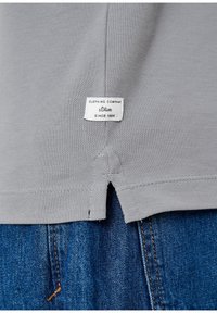 T-shirt en coton gris avec une surface légèrement texturée, des fentes latérales à l'ourlet et une étiquette s.Oliver cousue dans le dos. Jeans en denim visibles.