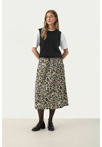 Un haut sans manches en tricot noir porté sur une chemise blanche à manches courtes, associé à une jupe maxi beige à imprimé léopard et des mocassins noirs.
