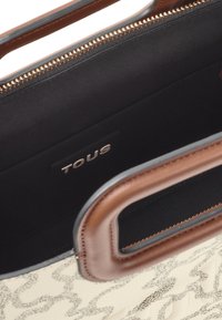 Brązowa skórzana torba z fakturowanym kremowym wzorem, zamek błyskawiczny i czarne materiałowe wnętrze. Wewnątrz znajduje się srebrna naszywka z logo.