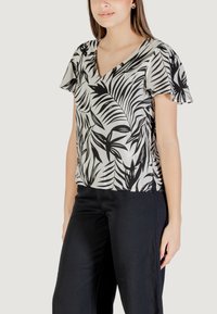 Blusa a maniche corte bianca e nera con scollo a V e motivo a foglie tropicali, realizzata in tessuto leggero, abbinata a pantaloni neri.