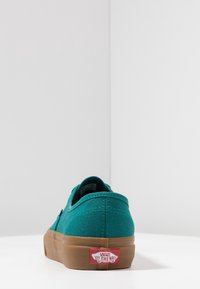 Baskets en toile bleu sarcelle avec une semelle en caoutchouc naturel de profil bas et le logo Vans caractéristique sur le talon. Vue arrière, mettant en avant un design minimaliste.