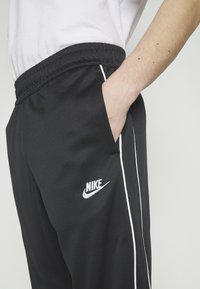 Svarta Nike-byxor med vita sidosträck och logotyp. Har elastisk midja och sidofickor. Materialet verkar slätt och lätt.