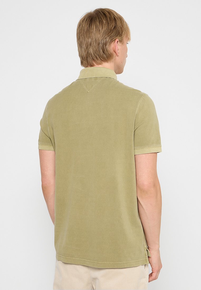 Camisa polo de manga corta en algodón verde oliva. Presenta un cuello clásico, detalle de costura en la parte posterior y aberturas laterales en el dobladillo para facilitar el movimiento.