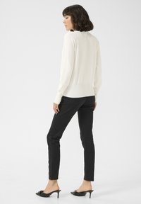 Witte lange mouwen top en zwarte slim-fit broek. De top heeft een gladde textuur; de broek heeft klassieke zakken. Zwarte open teen hoge hakken.