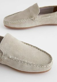 Des mocassins en daim de couleur gris clair. Présentent des détails cousus et une texture douce. Bout arrondi et design minimaliste avec une semelle beige.