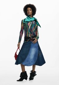 Pull tricot multicolore à manches longues, associé à une jupe en denim patchwork. Comprend des bottines noires et un petit sac à main rouge.