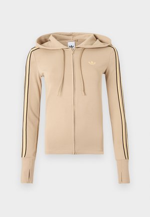 Beežzipiga nihkega materjaliga pusak, millel on mustad ja kollased küljepidemed, kapuuts ning väike kuldne logo rinnal.