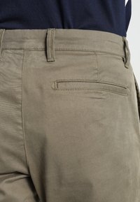 Pantaloni khaki con una texture del tessuto liscia, tasca posteriore standard e passanti per cintura, caratterizzati da un design semplice e minimalista.