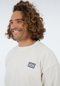Witte fleece sweatshirts met een ronde hals, voorzien van een blauw geborduurd logo op de linkerkant van de borst en een gestructureerde stof.