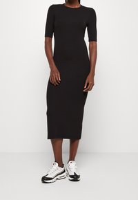Robe midi noire côtelée avec des manches courtes, design ajusté, texture lisse, associée à des baskets de sport blanches et noires.