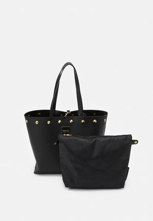 Zwarte draagtas met gouden studs en handvatten, vergezeld van een kleinere zwarte ritsportemonnee voorop op een effen achtergrond.