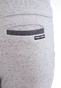 Acercamiento de un bolsillo de pantalón de tela gris jaspeada con un ribete negro y una etiqueta "TUMBLE 'N DRY" en el borde del bolsillo.