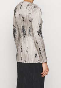 Blusa a maniche lunghe in morbido tessuto beige chiaro plissettato, con motivo floreale nero. Tessuto liscio con una silhouette sagomata e scollatura rotonda.