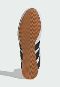 Schwarze und weiße Sneaker-Sohle mit strukturiertem Gummiprofil, das ein wellenförmiges Muster und drei schwarze Streifen an der Seite aufweist.