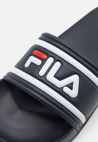 Infradito blu navy con ampia fascia caratterizzata da dettagli bianchi e un logo sollevato rosso e bianco. Suola in gomma testurizzata per una buona aderenza.