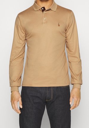 Polo à manches longues de couleur beige, avec un col marron et un petit logo brodé sur la poitrine. Matière en coton, coupe ajustée.